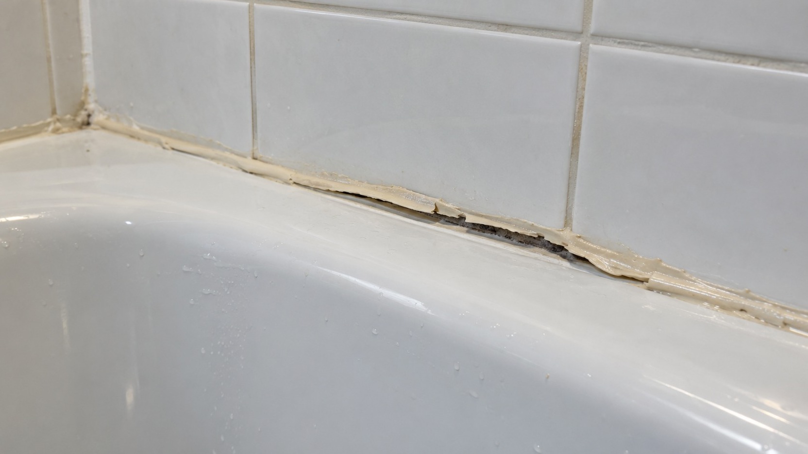 Junta de bañera con un cordón de silicona reciente que se separa de la superficie y deja visible una zona húmeda