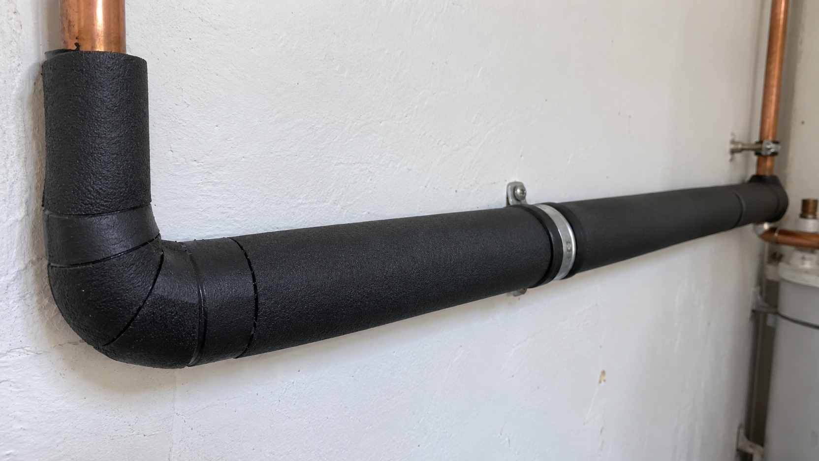 Tubería de agua caliente aislada que recorre una pared interior desde un termo eléctrico hasta el baño de una vivienda